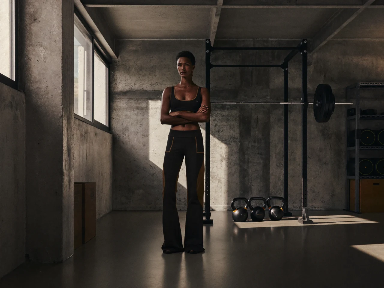 Spazio di allenamento in cemento grezzo con rack in acciaio, bilanciere e kettlebell allineati.