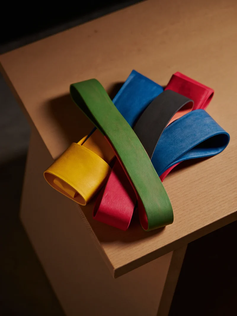 Bande elastiche colorate disposte a ventaglio su una panca di legno.